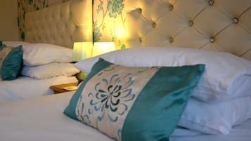 A hotel room with a tufted headboard, a bed with white and teal bedding, and a floral wallpaper design.