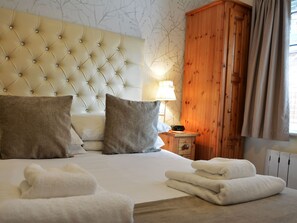 A neatly made bed with white linens and two pillows, a wooden nightstand with a lamp, and a wooden wardrobe. - Ashlea Guest House (Banbury)