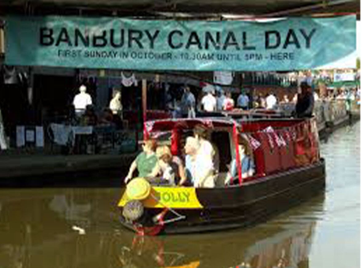 Un bote con un cartel que dice "BANBURY CANAL DAY" y una señal amarilla que dice "OLLY".