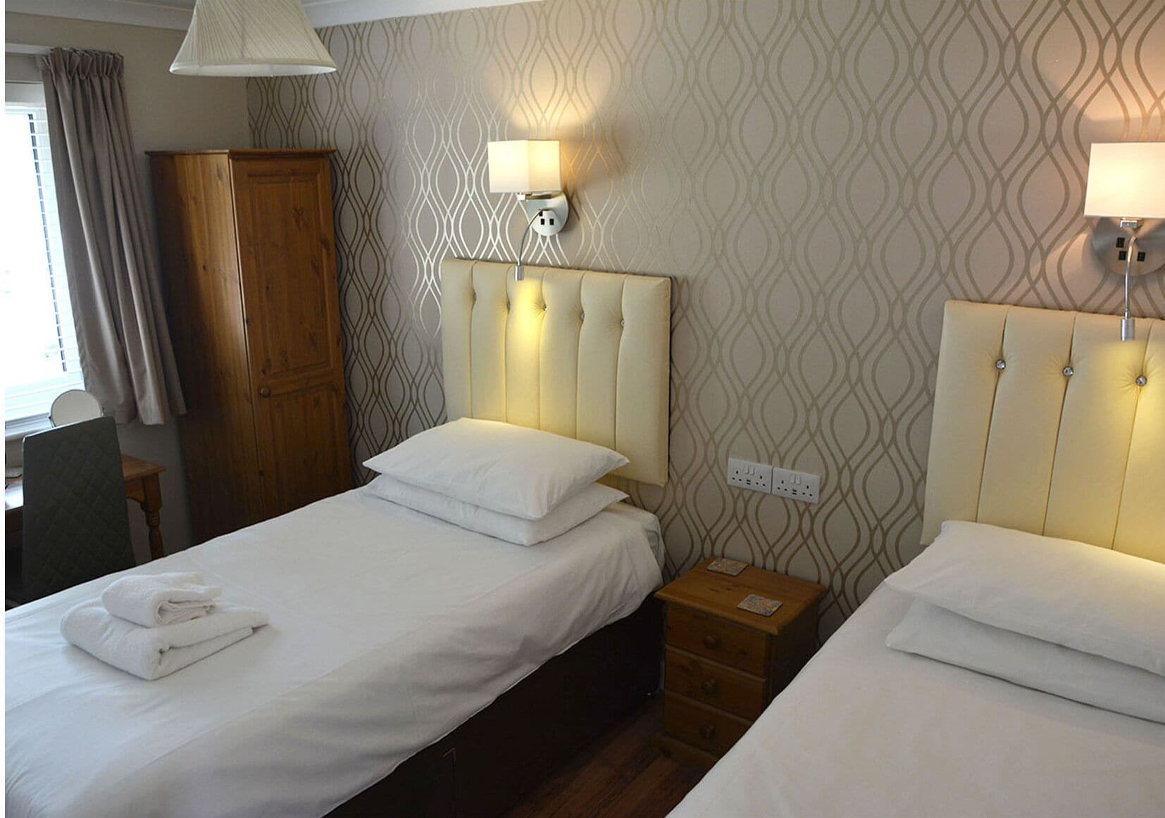 Habitació d'hotel amb dos llits, un armari de fusta, un escriptori i una làmpada.