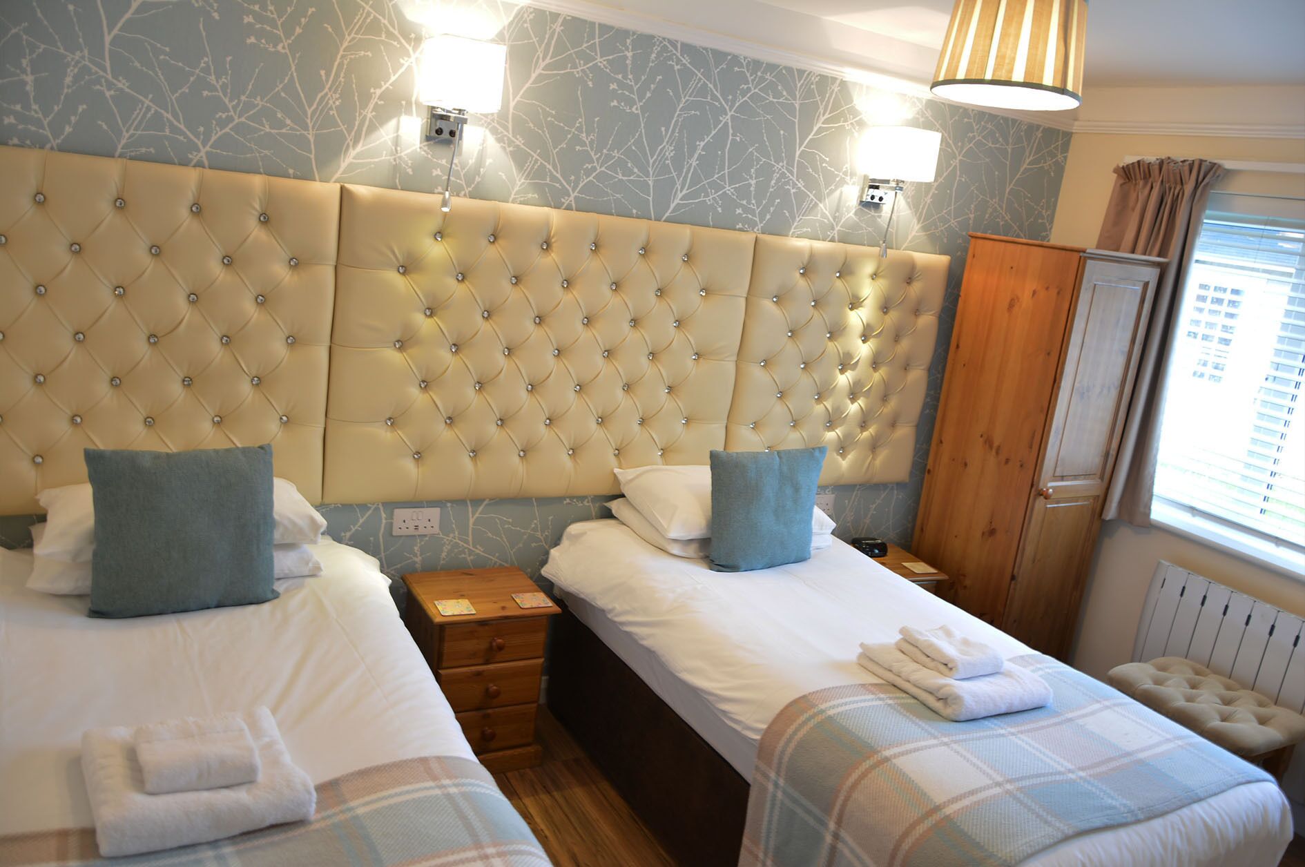 Habitación de hotel con dos camas, un armario de madera y una ventana con cortinas.