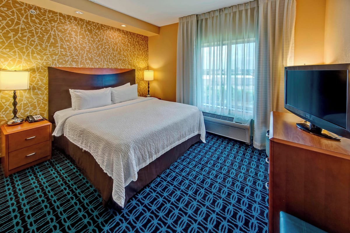 A hotel room with a large bed, a TV, a desk, and a window with curtains.