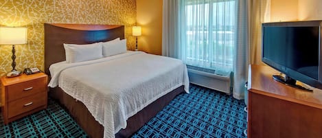 A hotel room with a large bed, a TV, a desk, and a window with curtains.
