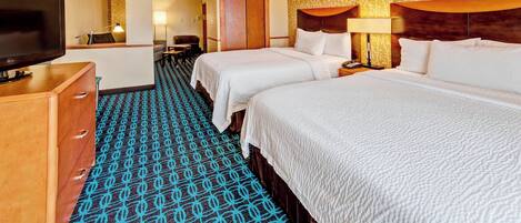 A hotel room with two beds, a TV, a desk, and a patterned carpet.
