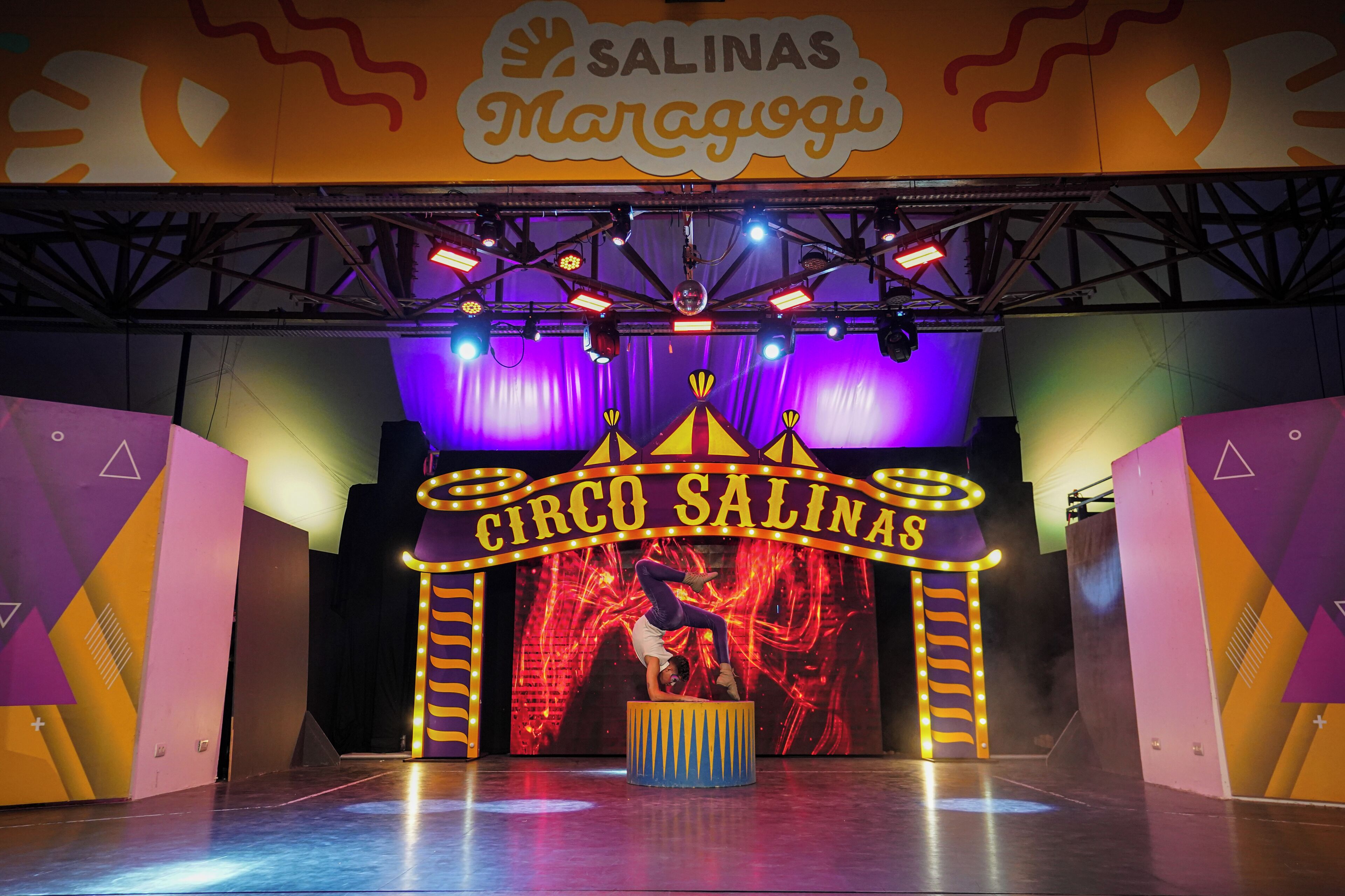 A circus-themed stage with a performer, a sign reading 'CIRCO SALINAS,' and a large, illuminated tent structure.
