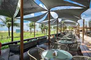 An outdoor seating area with wicker furniture and tables, shaded by large umbrellas, overlooking a beach. - Salinas Maragogi All Inclusive Resort (Maragogi)