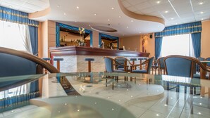 A modern hotel lobby with a bar area, seating arrangements, and a marble floor. - Hotel Astir Palace (Zakynthos)
