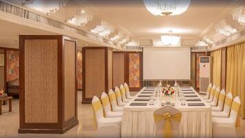 A formal dining room with a long table set for a banquet, flanked by tall wooden panels and a chandelier.