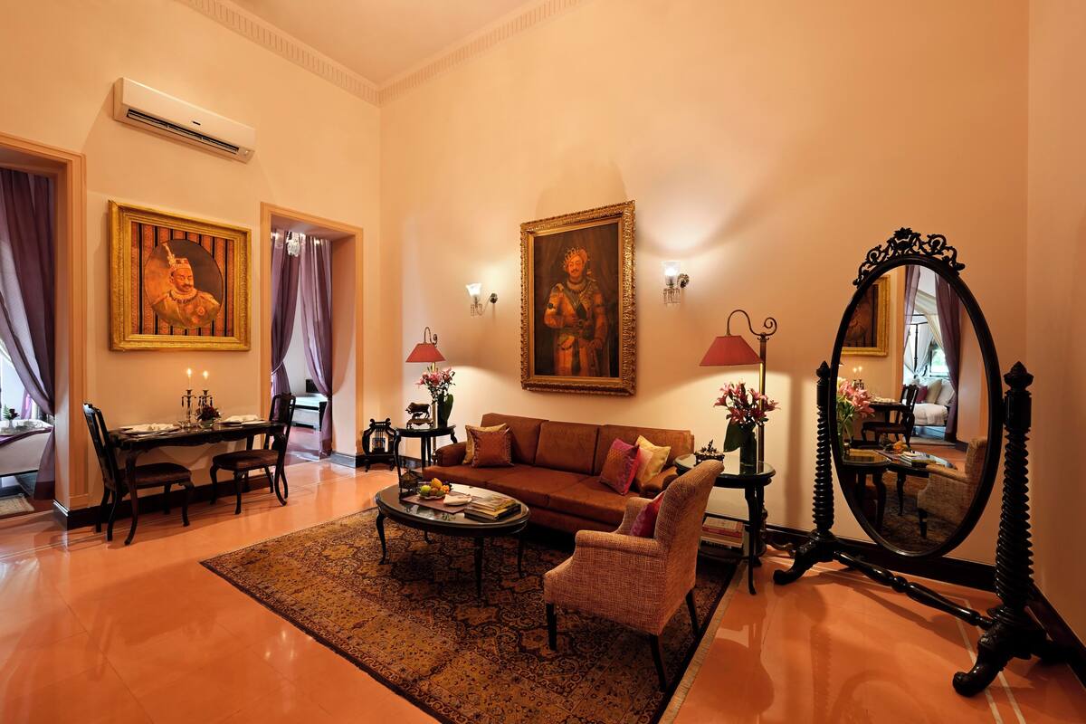 Una sala de estar bien amoblada con un sofá, sillones, una mesa de centro y una mesa de comedor con sillas. Hay dos lámparas de pared, un espejo grande y dos cuadros enmarcados.