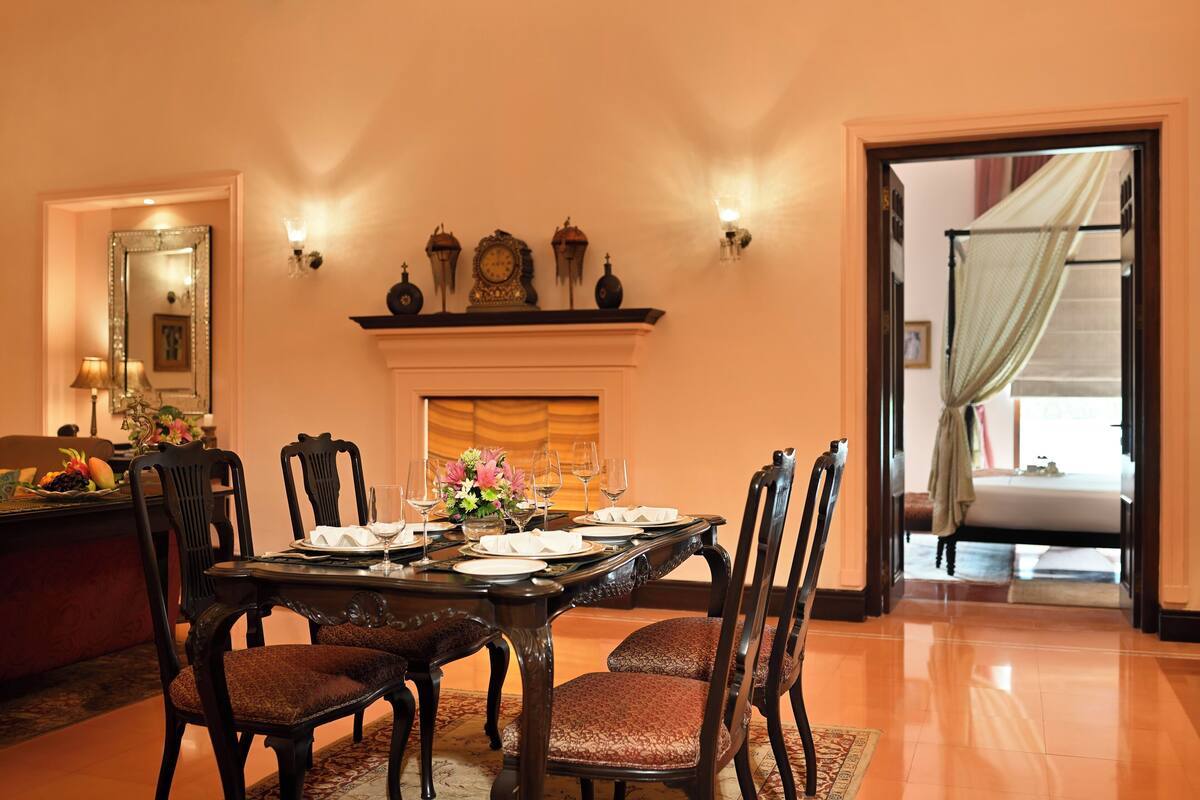 Comedor con una mesa de madera dispuesta para cuatro personas, flanqueada por sillas con asientos acolchados. Se observa una chimenea con repisa sobre la mesa.