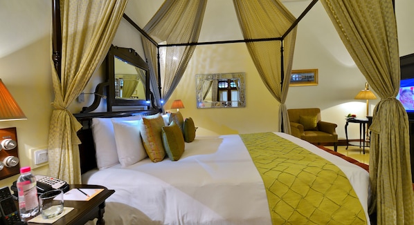 Habitación de hotel con cama con dosel, una mesita de noche con lámpara, una silla y un televisor.