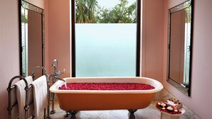 Un baño con una bañera independiente llena de pétalos de rosa, un perchero y una mesita de noche con artículos de aseo.