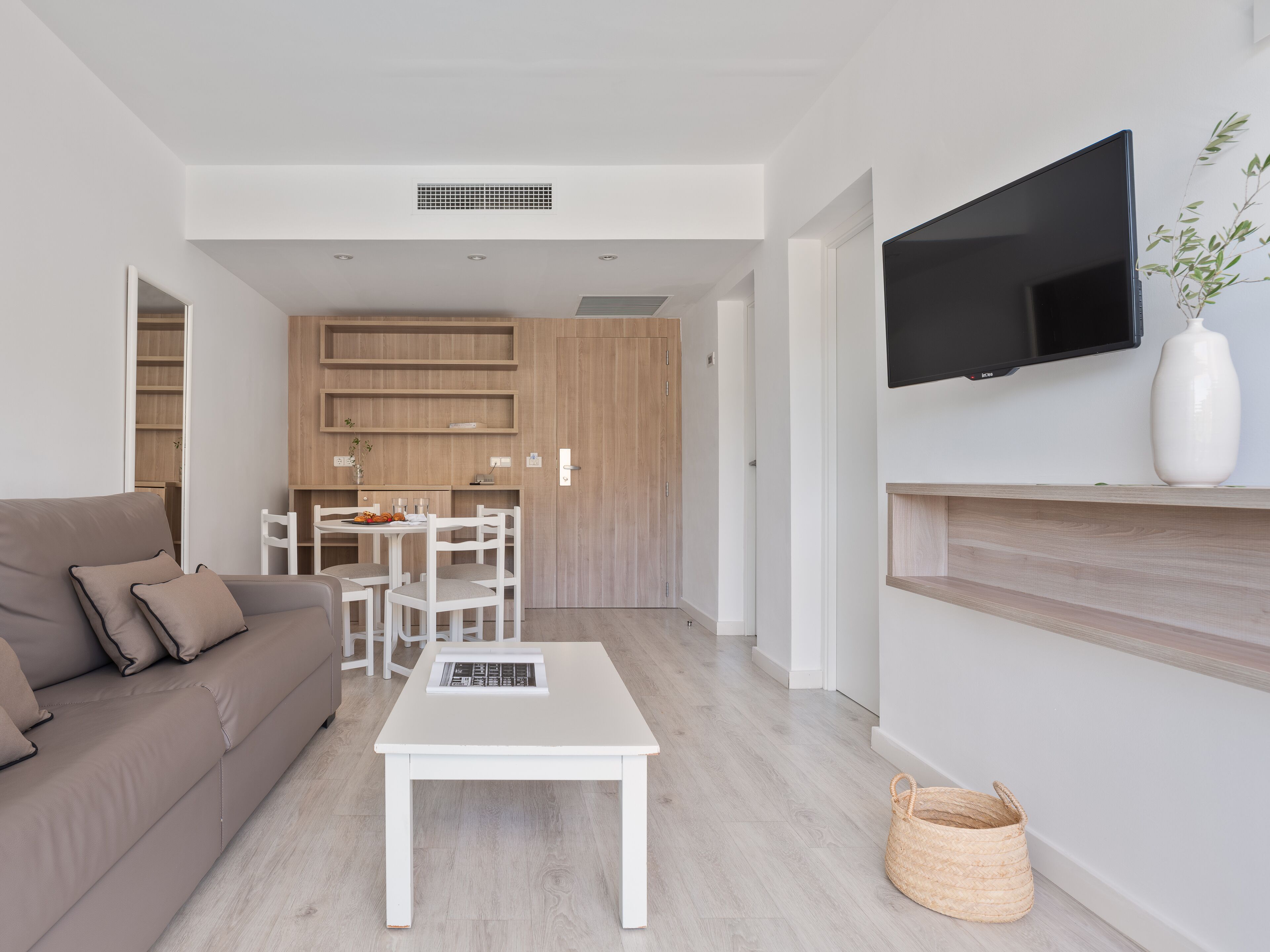 A modern living room with a sofa, a dining table, and a TV mounted on the wall.