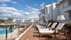 A poolside area with lounge chairs, a pool, and a view of a hotel building. - Puerto Azul Suite Hotel (Pollenca)