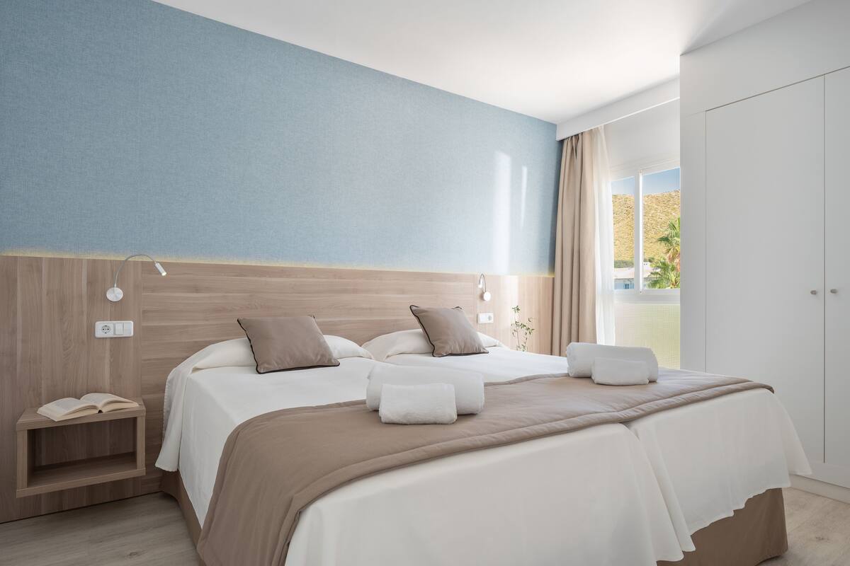 Une chambre d’hôtel moderne avec un grand lit, des tables de chevet et une vue sur un espace paysager aménagé.