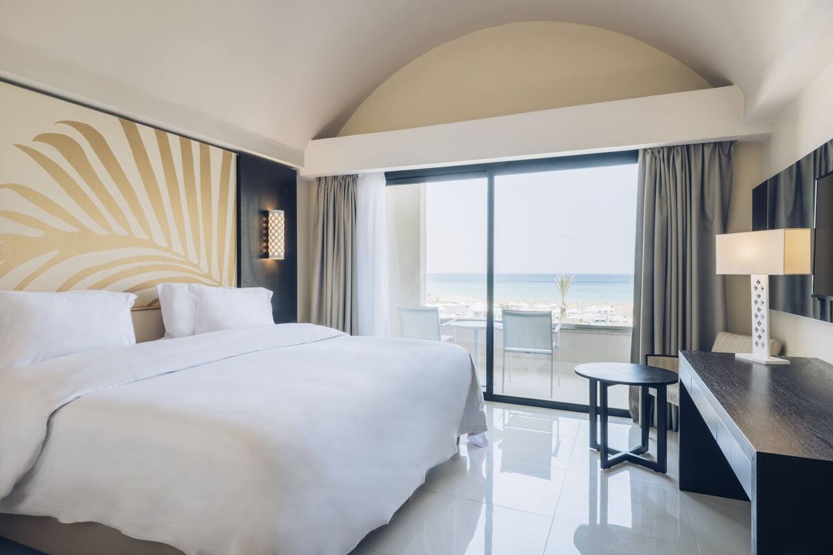 A hotel room with a large bed, a desk, and a view of the beach.