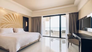 Een moderne hotelkamer met een groot bed, een bureau, een flatscreen-televisie en een balkon met uitzicht op zee.