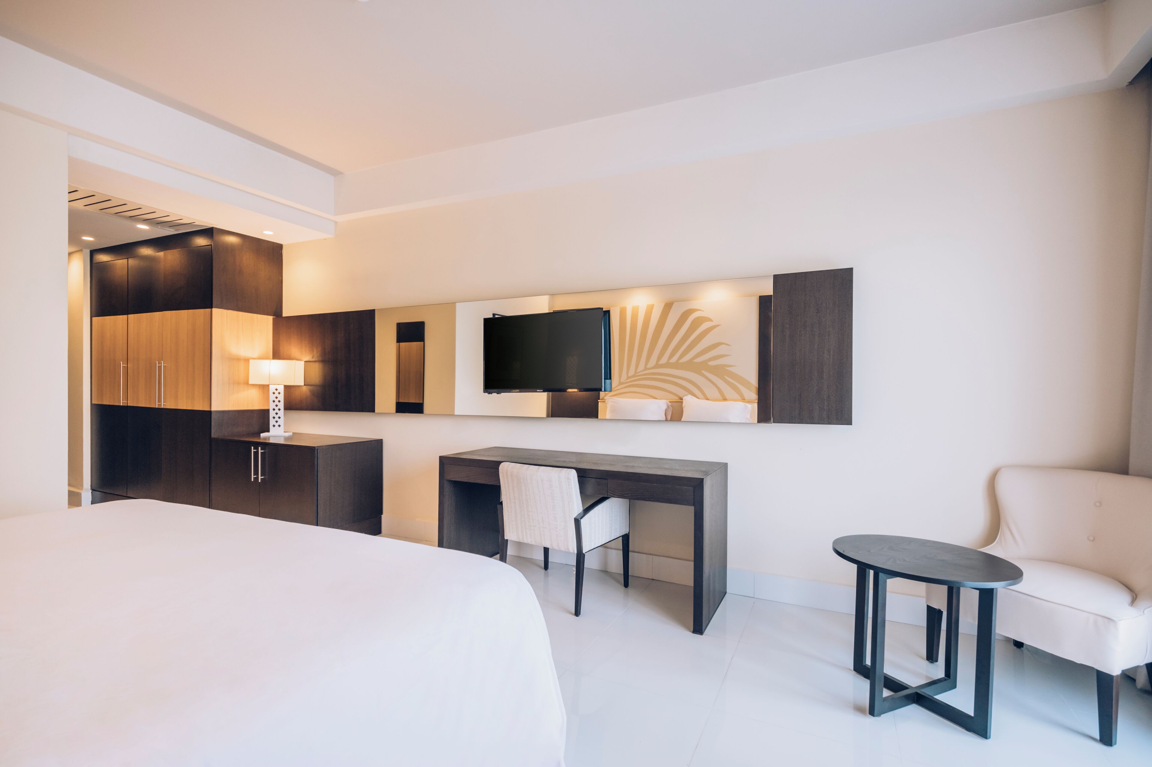 Ein modernes Hotelzimmer mit einem großen Bett, einem Schreibtisch, einem Stuhl, einem kleinen Tisch und einem an der Wand befestigten Fernseher.