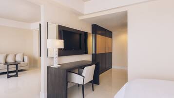 A modern hotel room with a dark wood desk, a chair, a flat-screen TV mounted on the wall, a sofa, and a bed.