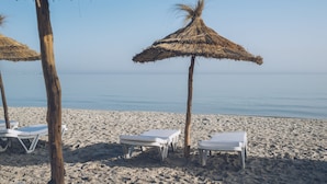 Een strand met witte ligbedden en rieten parasols.