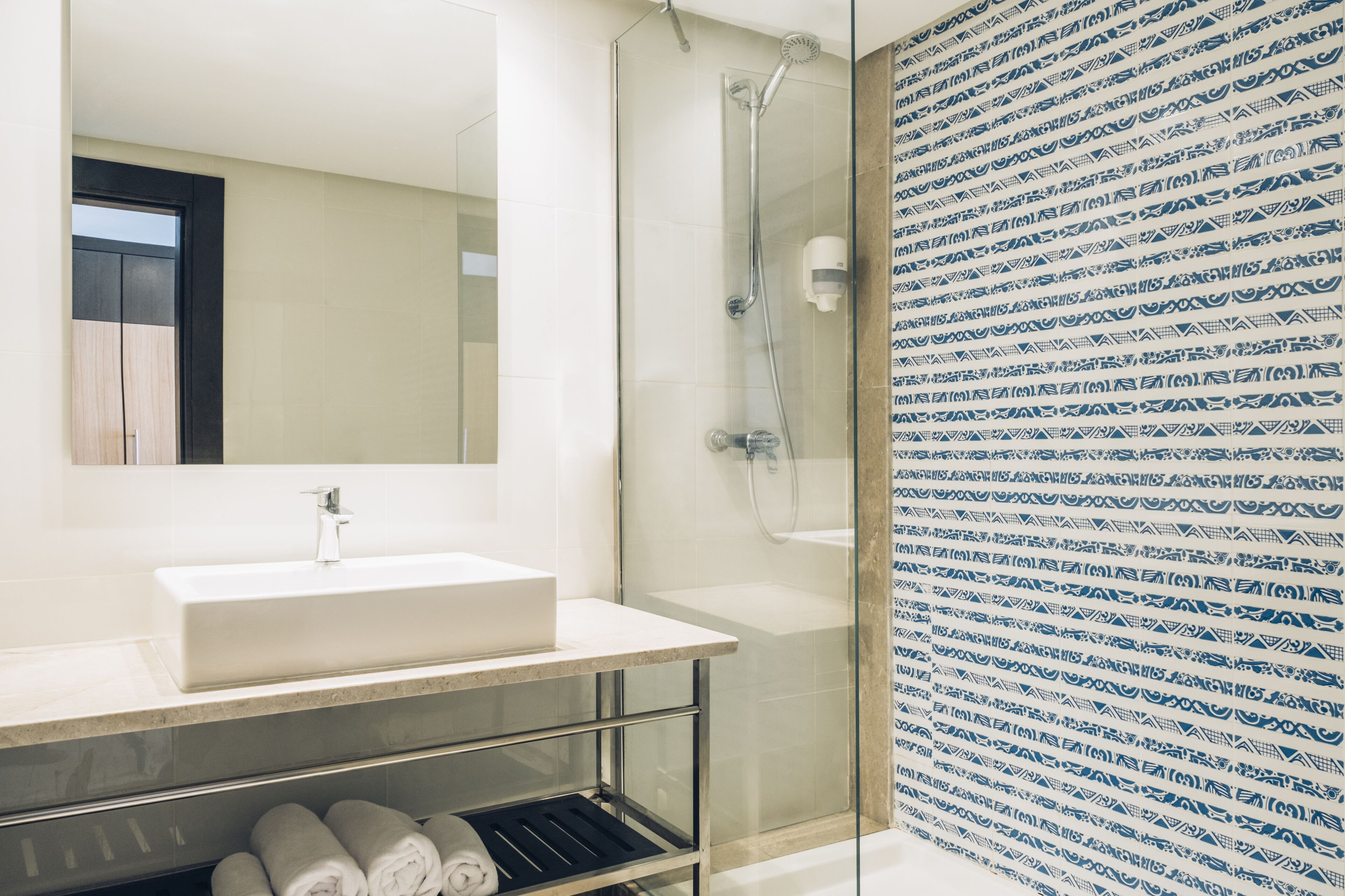 Ein modernes Badezimmer mit einem großen Spiegel, einem weißen Waschbecken und einer Duschkabine aus Glas.