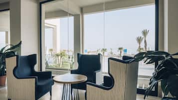 Eine moderne Hotelhalle mit großen Fenstern, zwei Sesseln, einem runden Tisch und Topfpflanzen.