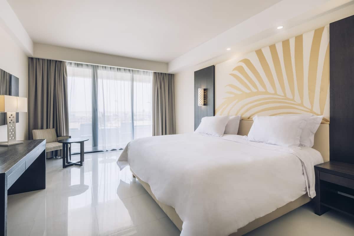 A modern hotel room with a large bed, a desk, and a view of the city.