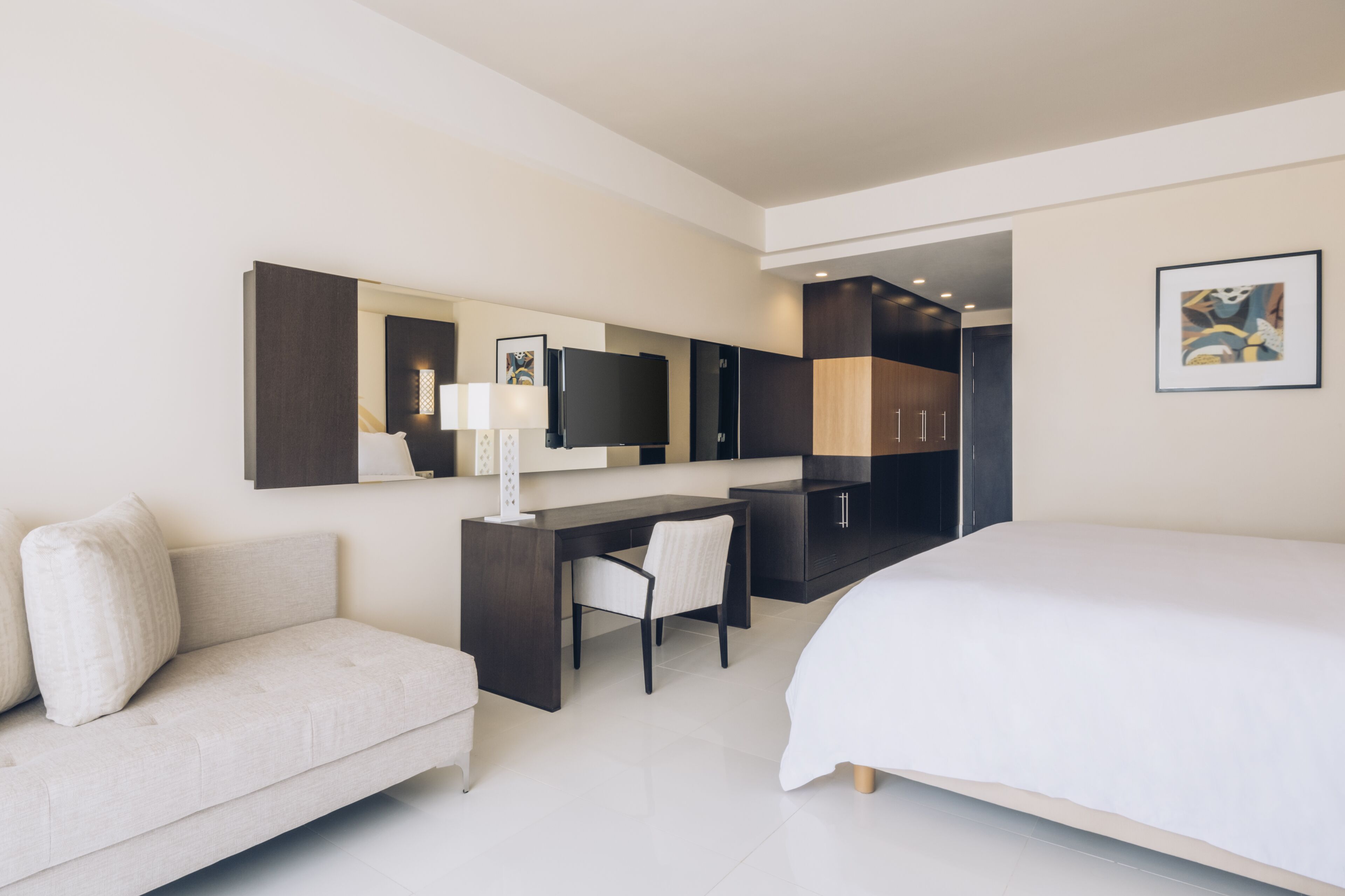 Ein modernes Hotelzimmer mit Bett, Schreibtisch, Stuhl, Sofa, Fernseher und Kleiderschrank.
