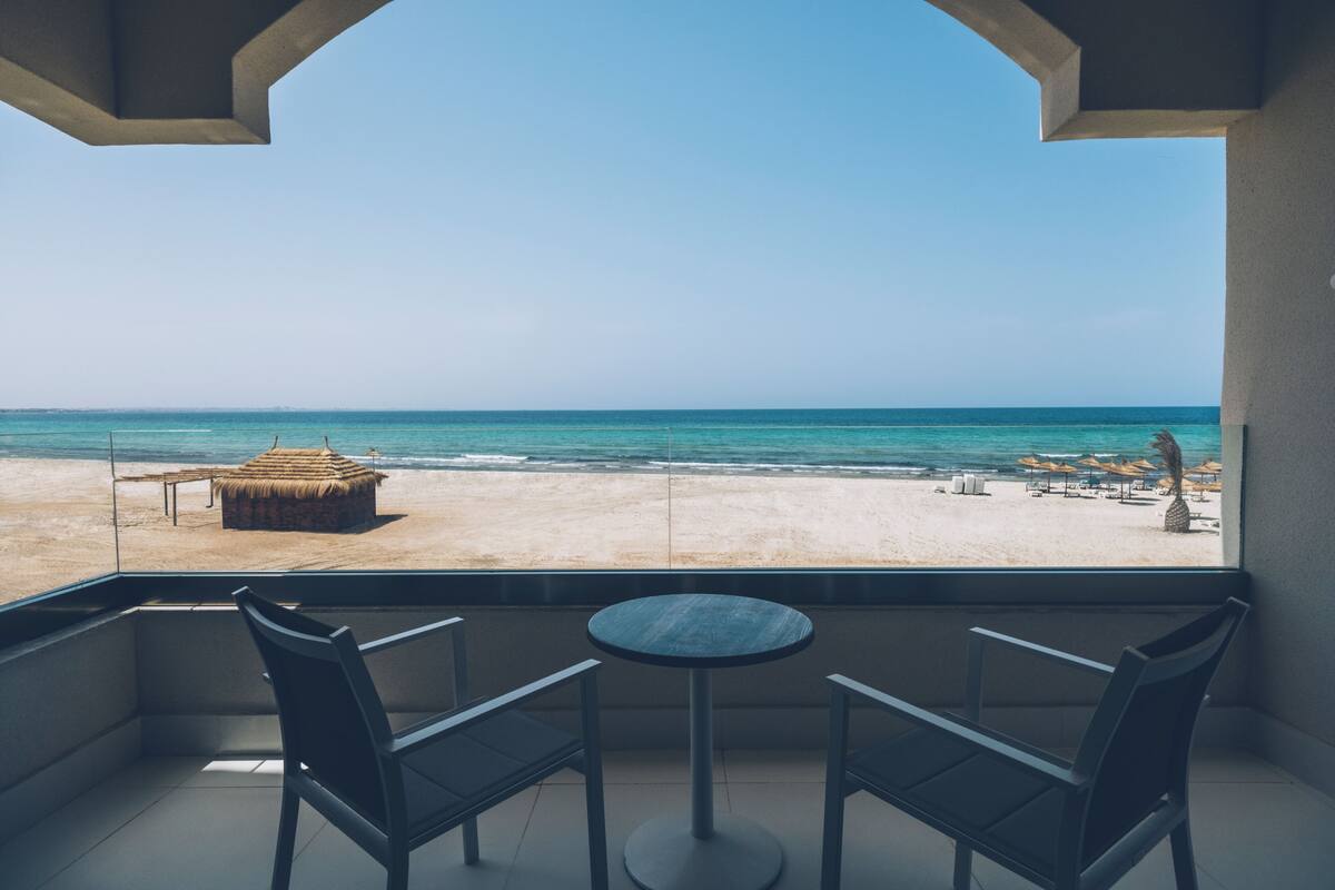 A balcony with a view of the beach, featuring a round table and two chairs.
