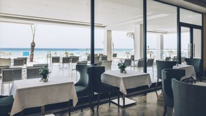 Een restaurant met tafels en stoelen, gericht op een zandstrand met de oceaan op de achtergrond.
