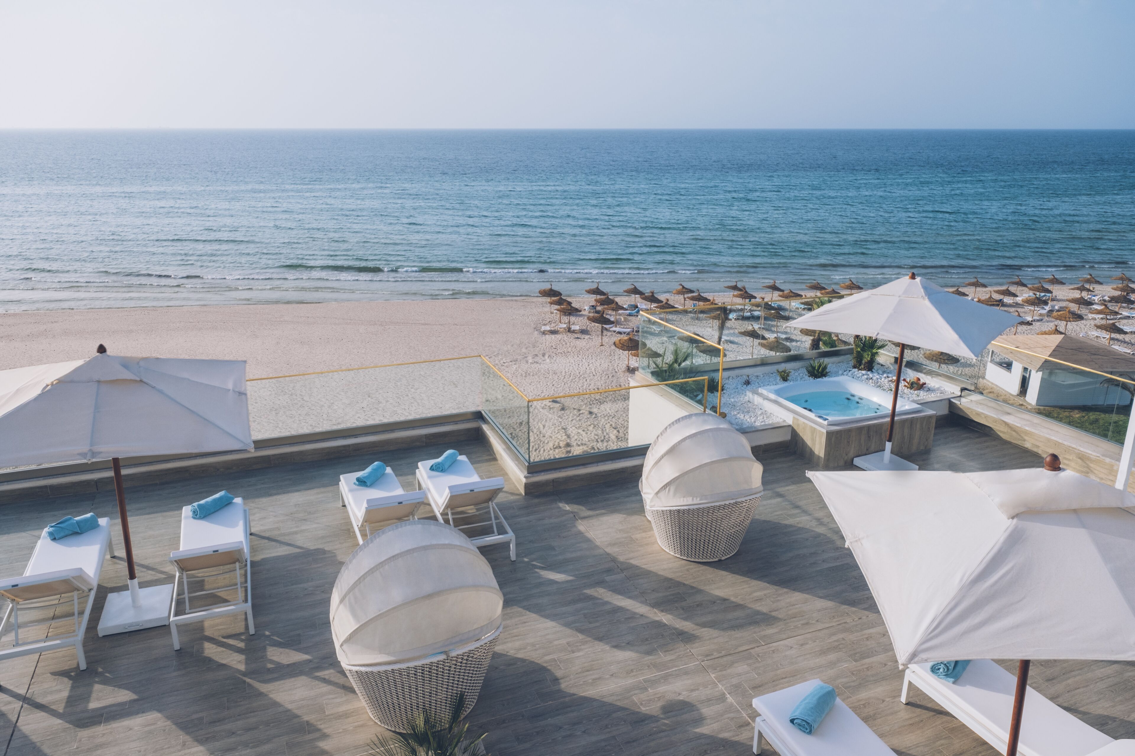 Een terras op het dak met lounge stoelen, parasols en uitzicht op het strand en de zee.