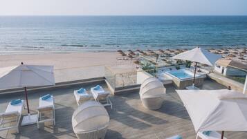 Een terras op het dak met lounge stoelen, parasols en uitzicht op het strand en de zee.