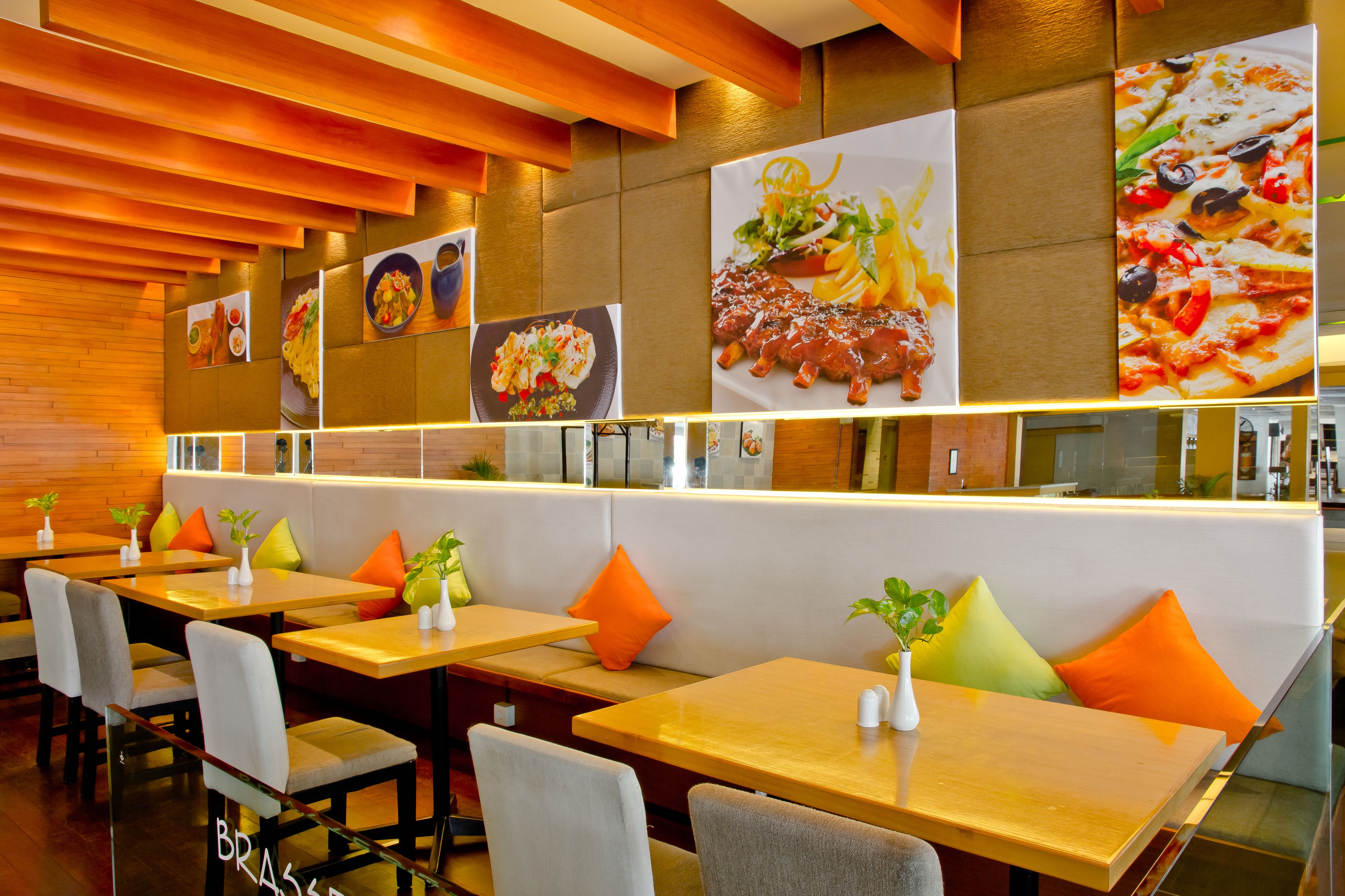 A restaurant with wooden tables and booths, orange cushions, and wall art of food.
