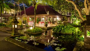 Ein Gebäude im traditionellen Stil mit Ziegeldach, umgeben von einem Garten mit Teich und unterschiedlichen Pflanzen.