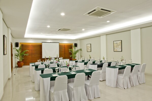 A conference room with multiple tables, white chairs, and green tablecloths.