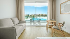 Een moderne hotelkamer met een bank, een klein rond tafeltje, twee stoelen en een grote schuifglazen deur die uitkomt op een zwembad.