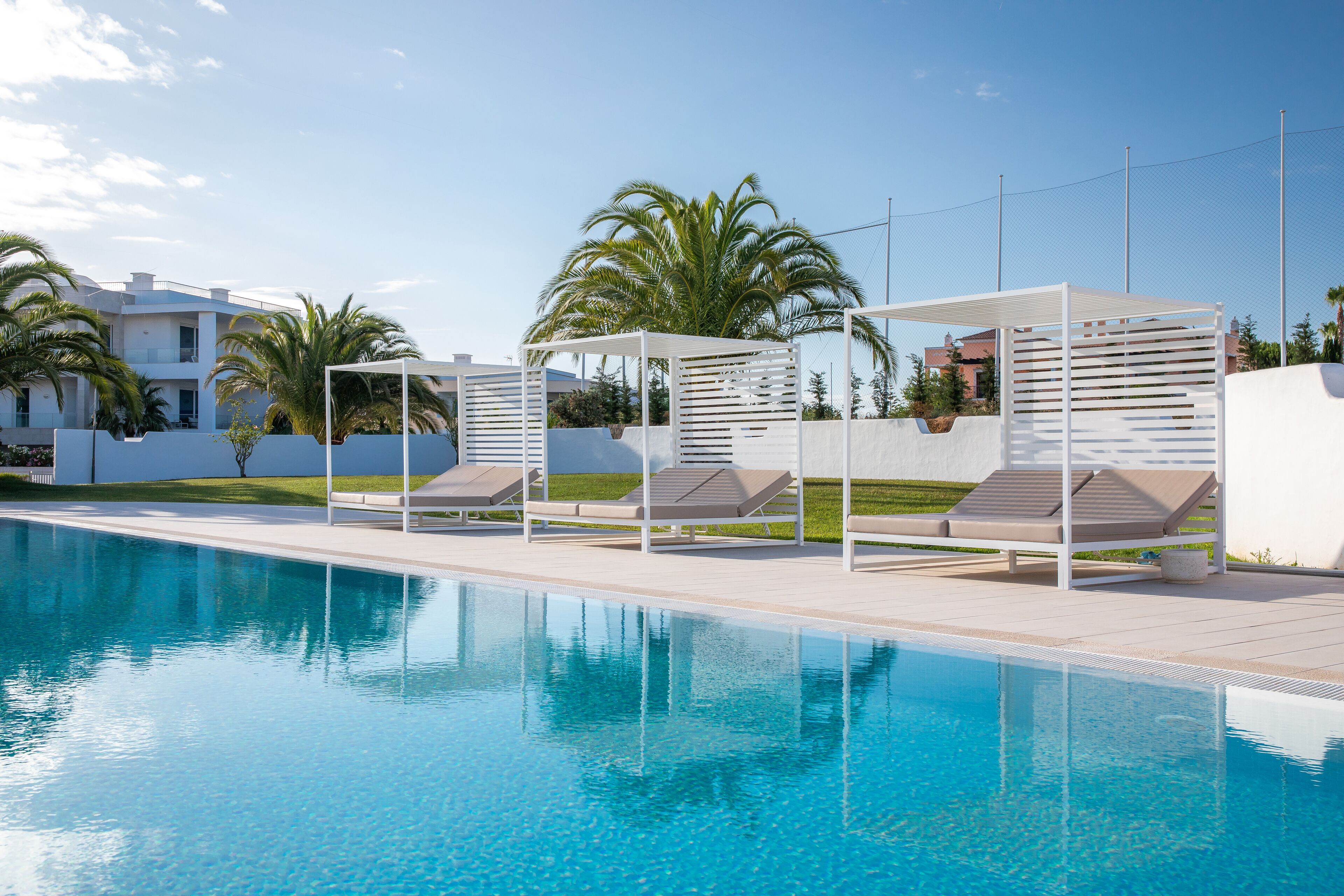 Una piscina con sillones de descanso y una pérgola.