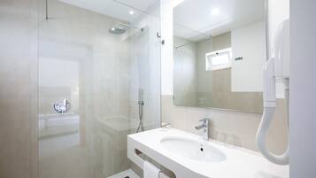 Un baño moderno con ducha envuelta en vidrio, lavamanos blanco y un espejo grande.
