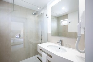 Un baño moderno con ducha envuelta en vidrio, lavamanos blanco y un espejo grande.