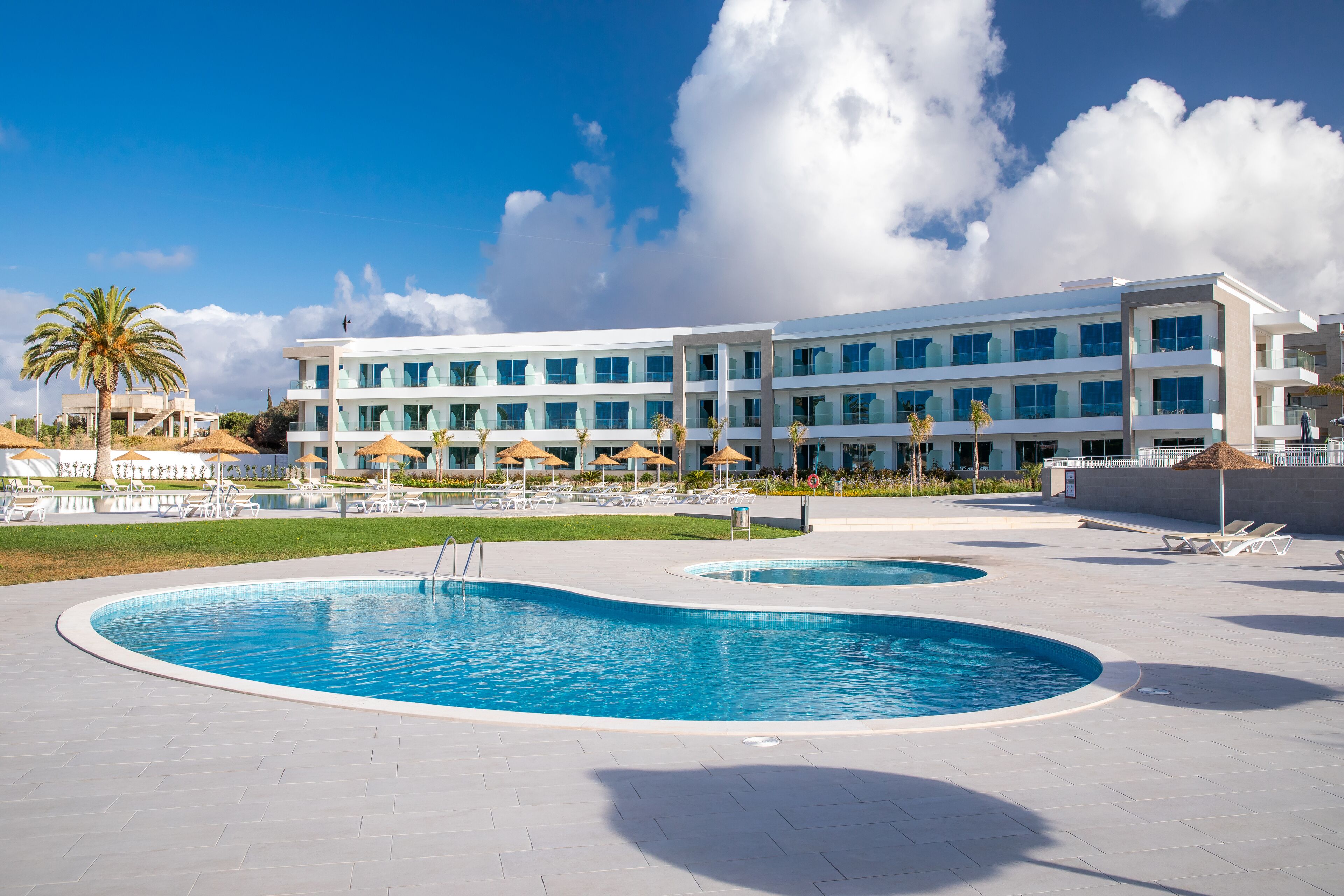A modern hotel with a large pool area, sun loungers, and umbrellas.