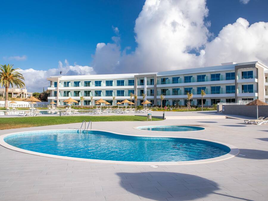 Un hotel moderno con una grande area piscina, lettini e ombrelloni.