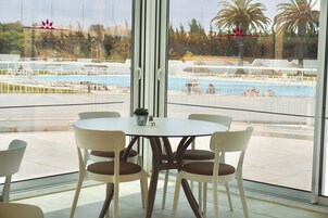 A dining area with a round table and chairs, a view of a pool, and a balcony with a railing.