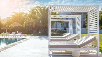 Un área junto a la piscina con sillones de descanso y una pérgola.