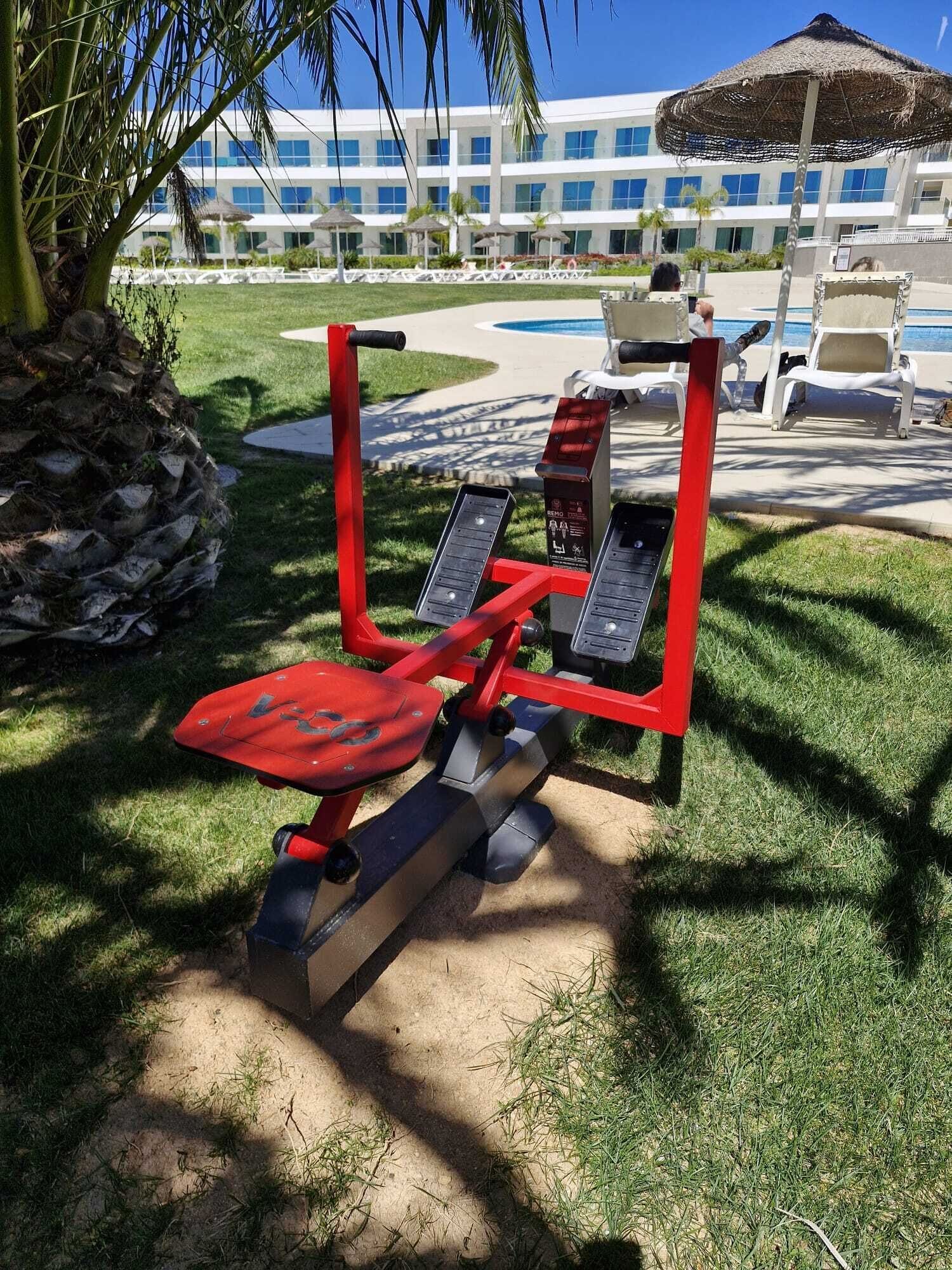 Des appareils de musculation en plein air, une piscine et un bâtiment doté de nombreuses fenêtres.