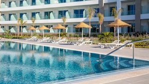 Una piscina con sillas de descanso y sombrillas, rodeada por un edificio moderno con varios balcones.
