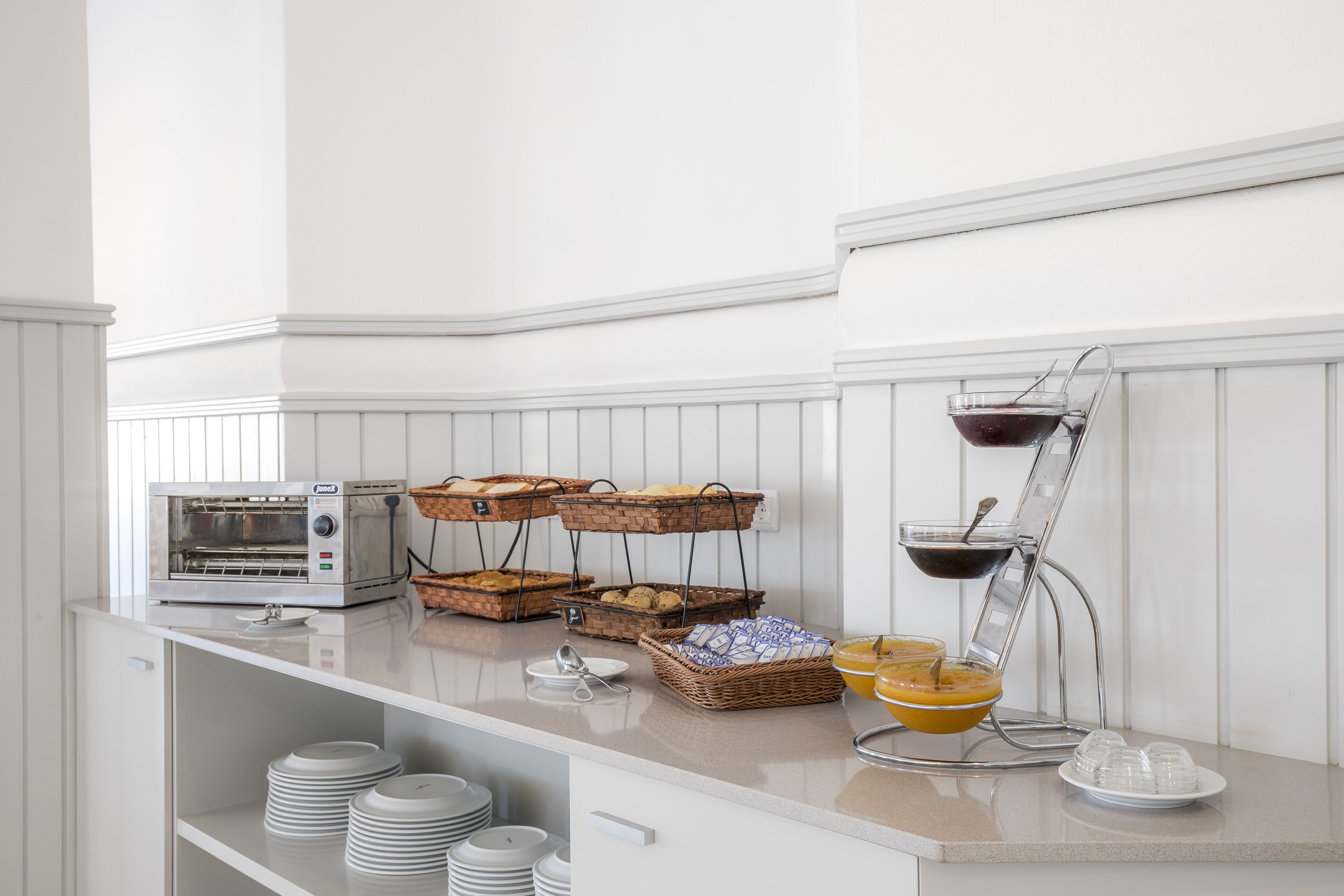 A buffet setup with a toaster oven, baskets of bread, and a juice dispenser.