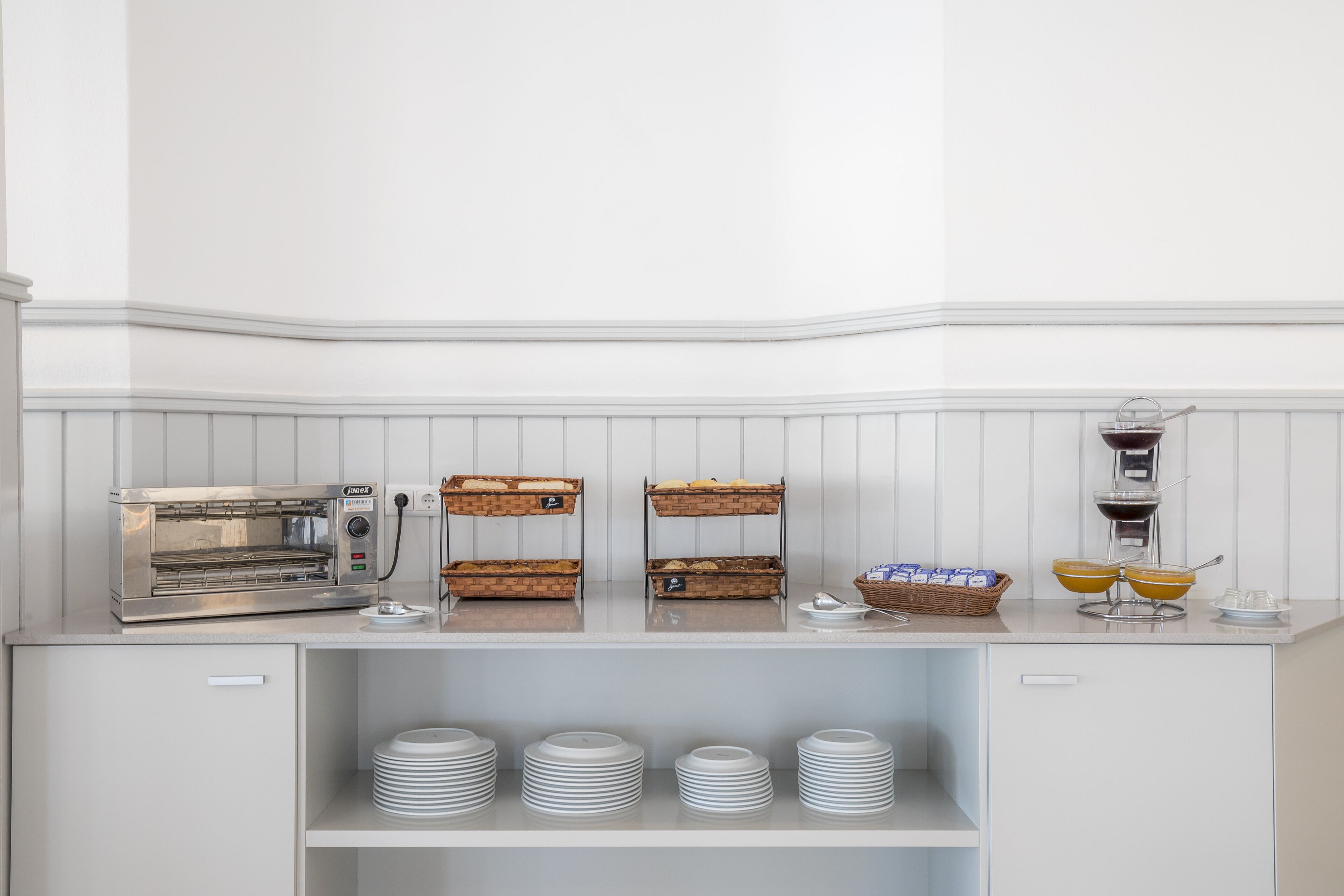 A breakfast bar with a coffee machine, bread baskets, and stacked plates.