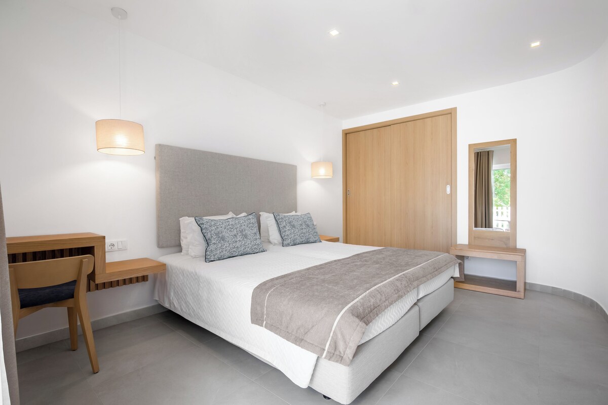 A modern bedroom with a bed, bedside tables, a desk, and a wardrobe.