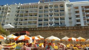 Un hotel con varios balcones, mobiliario exterior con sombrillas y una vista despejada de la fachada del edificio.