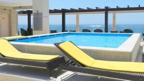 Un área de piscina con vista al mar, que incluye una piscina, sillas de descanso y una pérgola.